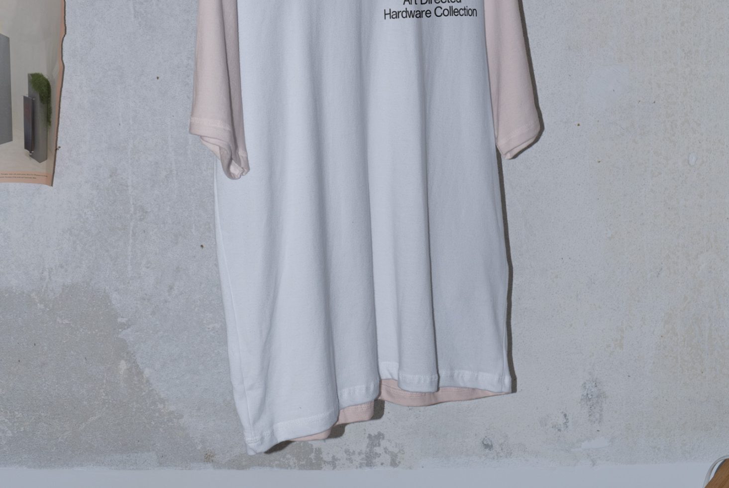 Three hanging t-shirts, white and pastel, text detail, against textured wall, realistic apparel mockup for design presentation.